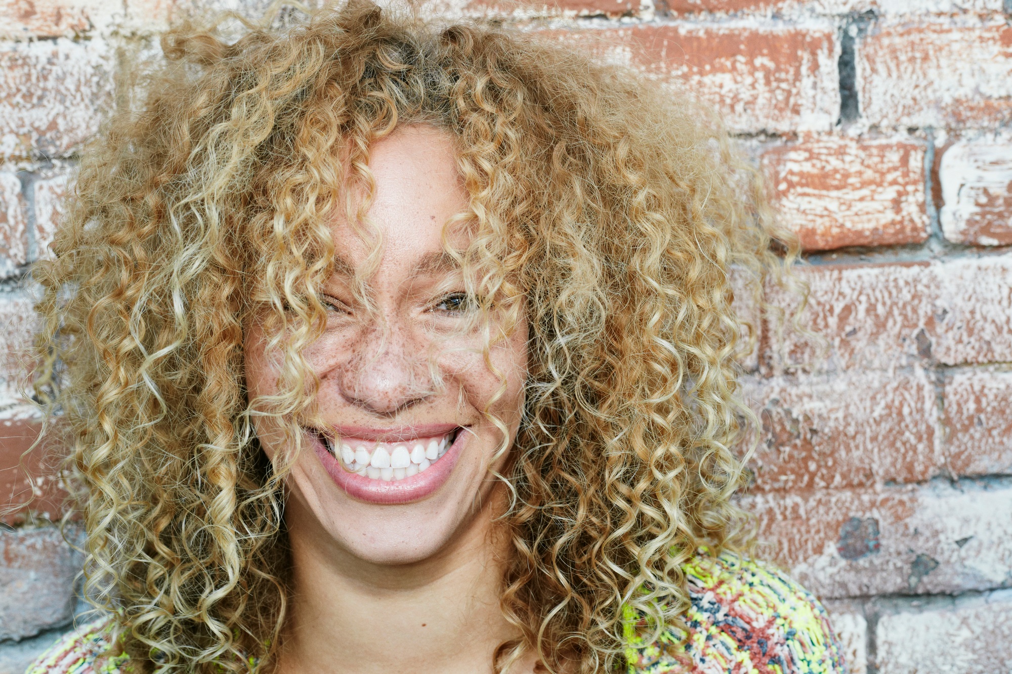Portrait of young smiling woman with long curly blond hair, looking at camera.